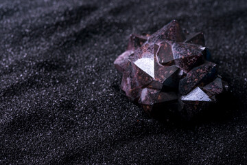 Red csemi-precious stone, druse on the black  sand. Close up.