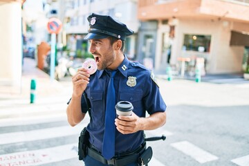 Young handsome hispanic policeman wearing police uniform smiling happy. Eating donut and drinking...