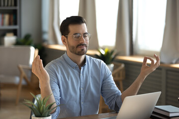 Serene office male employee sit at desk relaxing doing yoga, practice meditation to reduce stress...