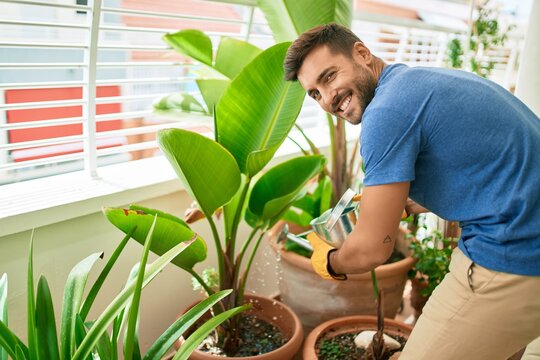 Young handsome man smiling happy caring plants using watering can at terrace