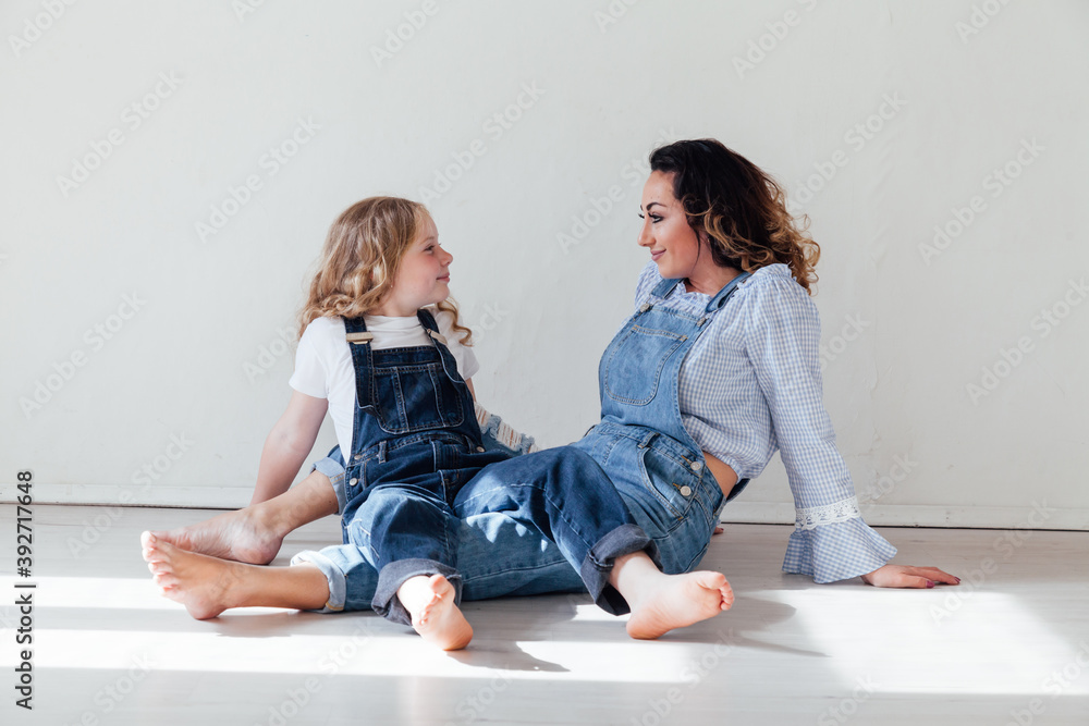 Wall mural mom brunette and daughter blonde in jeans sit on the floor