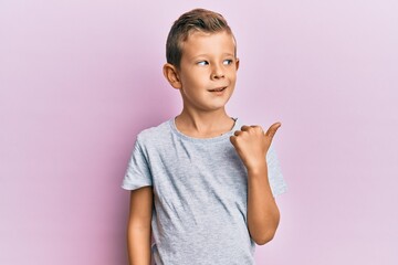 Adorable caucasian kid wearing casual clothes pointing thumb up to the side smiling happy with open mouth