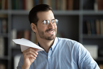 Naklejka premium Optimistic businessman in glasses looking away having fun in office folded paper into plane and launching, symbol of creativity at work, daydreaming about future vacation, career aspirations concept