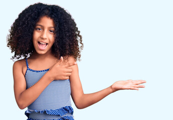 African american child with curly hair wearing swimwear amazed and smiling to the camera while presenting with hand and pointing with finger.