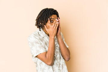 Young african american rasta man blink through fingers frightened and nervous.
