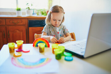 Toddler girl playing modelling clay in front of laptop