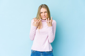 Young blonde woman isolated on blue background upset screaming with tense hands.