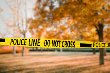 Yellow police tape isolating crime scene. Blurred view of autumn city park