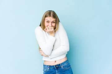 Young blonde woman isolated on blue background biting fingernails, nervous and very anxious.