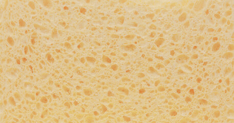 The pale yellow surface of a sponge, with many holes, also looking like the inside of crusty bread. Useful texture or backdrop.
