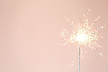 Bright burning sparkler on pink background, closeup. Space for text