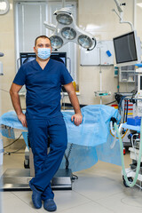 Fototapeta premium Young confident male doctor poses to the camera on modern surgery room background. Health care and life saving concept.