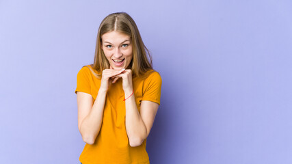 Young blonde woman isolated on purple background praying for luck, amazed and opening mouth looking to front.