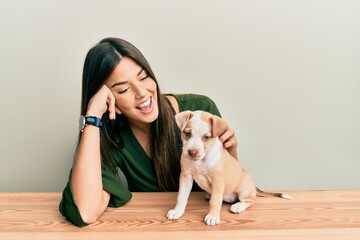 Young hispanic girl smiling happy and playing with dog sitting on the table over isolated white background.