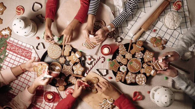 Family is decorating a traditional gingerbread. Xmas flat lay video. Christmas and New Year holidays mood. Group of people glaze a cookie. Top view of home table.
