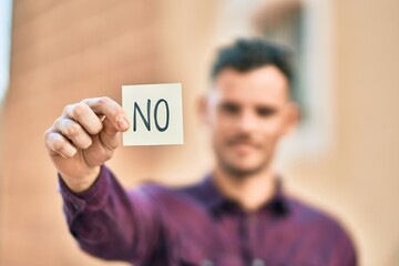 Young hispanic man with serious expression holding no reminder paper at the city.