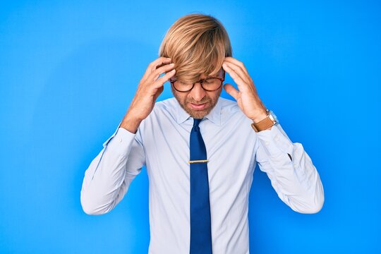 Young blond man wearing business clothes and glasses with hand on head for pain in head because stress. suffering migraine.