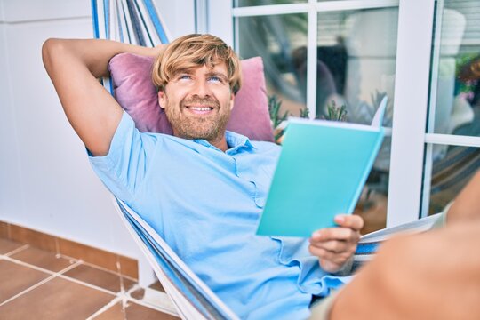 Middle age handsome man at the terrace of his house relaxing lying on a hammock reading a book