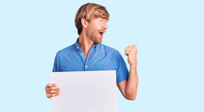 Handsome caucasian man with beard holding sale poster pointing thumb up to the side smiling happy with open mouth