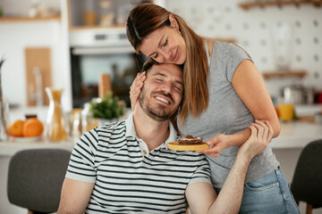 Fototapeta premium Young woman suprise her husband with cookie. Happy couple enjoying at home...