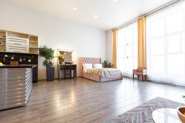 Contemporary ordinary design of spacious studio in soft warm colors. Simple furniture. Light large room with sunlight. Daytime. Tiled brown floor and white walls .