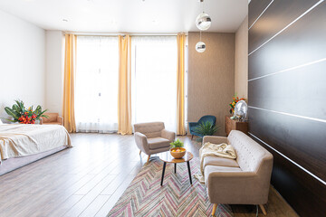 Contemporary ordinary design of spacious studio in soft warm colors. Simple furniture. Light large room with sunlight. Daytime. Tiled brown floor and white walls .