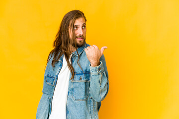 Young man with long hair look points with thumb finger away, laughing and carefree.