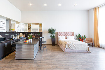 Contemporary ordinary design of spacious studio in soft warm colors. Simple furniture. Light large room with sunlight. Daytime. Tiled brown floor and white walls .