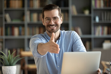 Human resource agent male recruiter sit at desk extends his hand to camera for handshake greeting applicant showing polite gesture start job interview in modern office. Welcoming, cooperation concept