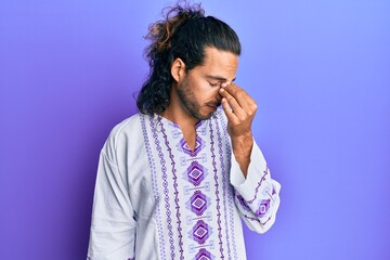 Young handsome man with long hair wearing bohemian and hippie shirt tired rubbing nose and eyes feeling fatigue and headache. stress and frustration concept.