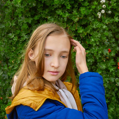 Beautiful teenage blonde schoolgirl in a blue and yellow coat in park in autumn