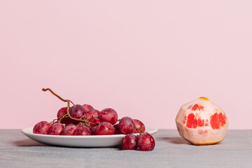 Close-up of a bunch of grapes and a peeled grapefruit on a pink background