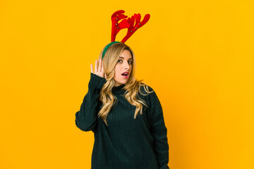 Young blonde caucasian woman wearing reindeer horns trying to listening a gossip.