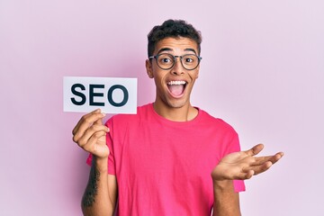 Young handsome african american man holding seo message paper celebrating achievement with happy...