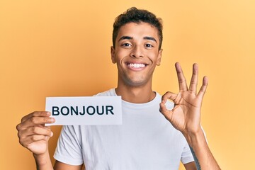 Young handsome african american man holding bonjour french greeting word doing ok sign with fingers, smiling friendly gesturing excellent symbol © Krakenimages.com