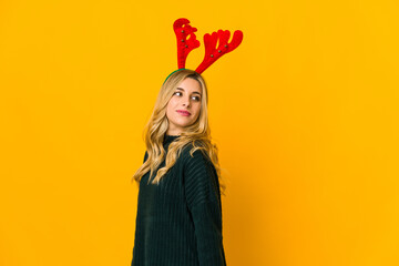 Young blonde caucasian woman wearing reindeer horns looks aside smiling, cheerful and pleasant.