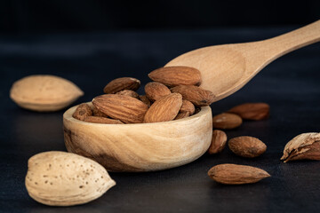 Almonds in a wooden bowl and on a wooden spoon on a black wooden table. CLose-up shot