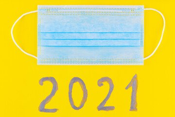 Text 2021 on a yellow background and surgical mask. Concept of the New Year with blue protective...