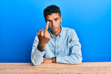Young handsome african american man wearing casual clothes sitting on the table showing middle...