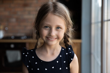 Headshot portrait of happy joyful little girl of primary school age with funny pigtails posing at...