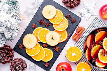 Cooking mulled wine with oranges, apples, anise and cinnamon for Christmas on pink table top, top view, flat lay