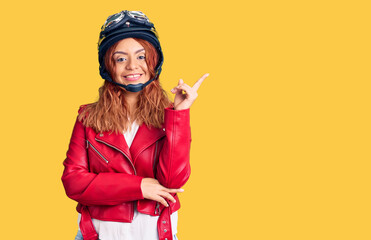 Young latin woman wearing leather jacket holding motorcycle helmet smiling happy pointing with hand and finger to the side