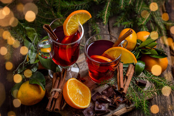 mulled wine with spices and fruits on a wooden table. Traditional hot drink for Christmas. Garlands, lighting 2 New Year's drinks in glass mugs.