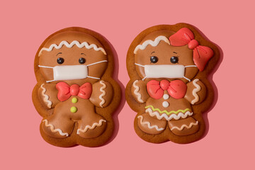 Christmas gingerbread man and woman in medicine mask on the rose background. Be responsible. Couple of gingerbread