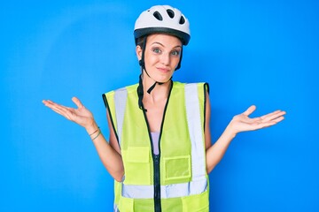 Young caucasian girl wearing bike helmet and reflective vest clueless and confused expression with arms and hands raised. doubt concept.