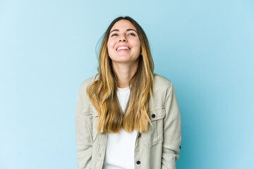 Obraz premium Young caucasian woman isolated on blue background laughs and closes eyes, feels relaxed and happy.