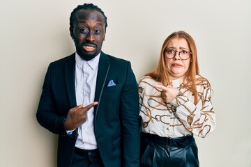 Young interracial couple wearing business and elegant clothes pointing aside worried and nervous with forefinger, concerned and surprised expression
