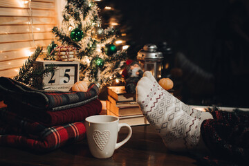 Feet in Christmas socks. Close up on feet. Winter and Christmas holidays concept. The cup of hot drink. Cozy scene. Background with christmas decor. Christmas background.