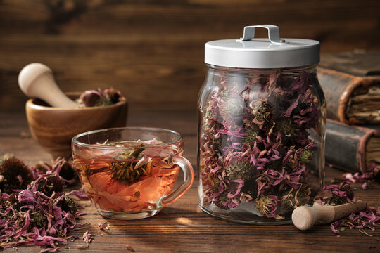 Cup of healthy echinacea tea, glass jar of dry coneflower herbs, wooden mortar and old books on table. - Powered by Adobe