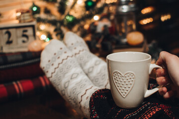 Feet in Christmas socks. Close up on feet. Winter and Christmas holidays concept. The cup of hot drink. Cozy scene. Background with christmas decor. Christmas background.